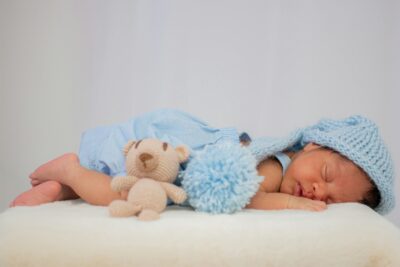 A serene image of a newborn sleeping in a blue outfit, adorned with a cute teddy bear.